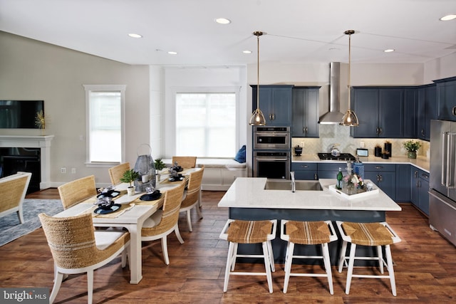 kitchen with a kitchen island with sink, wall chimney exhaust hood, decorative backsplash, dark hardwood / wood-style flooring, and stainless steel appliances