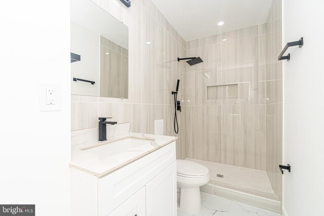 bathroom featuring a tile shower, vanity, and toilet