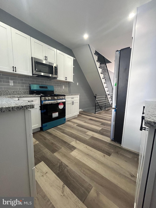 kitchen with appliances with stainless steel finishes, white cabinetry, dark wood-type flooring, backsplash, and light stone countertops