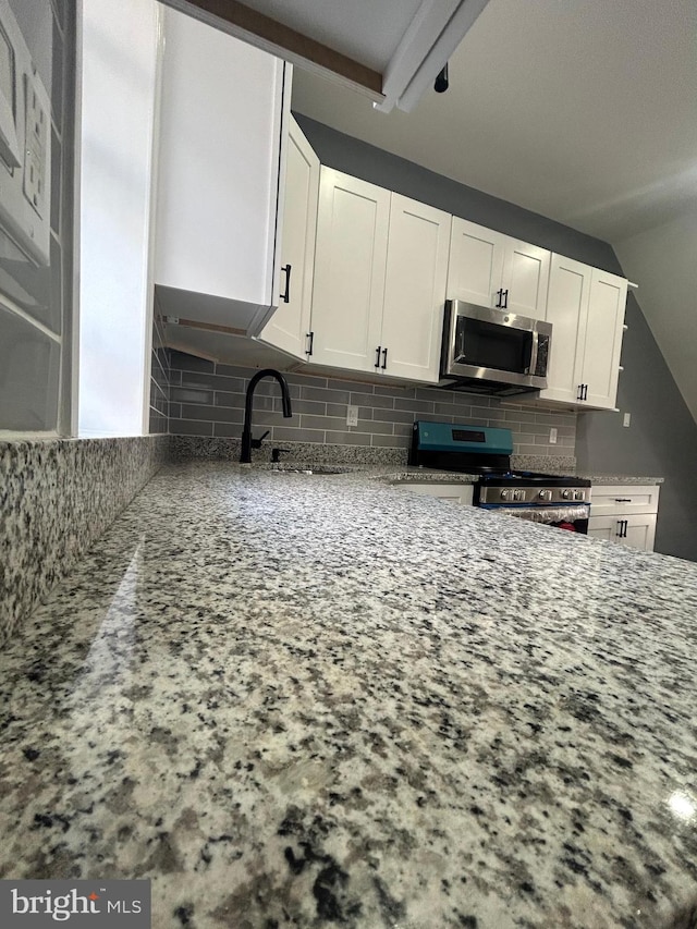 kitchen featuring white cabinetry, light stone counters, backsplash, stainless steel appliances, and sink