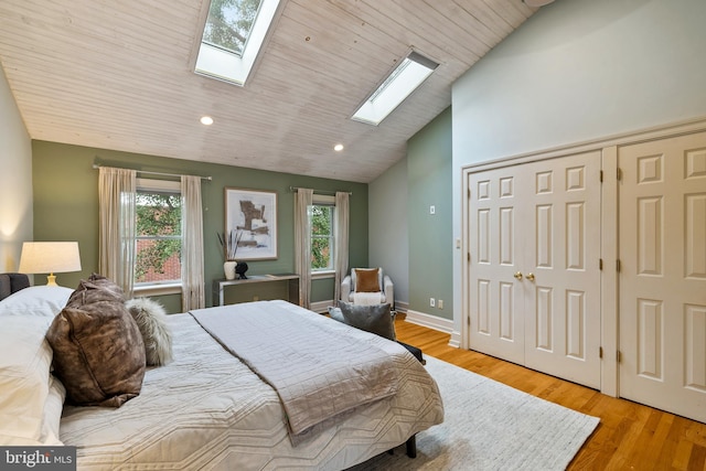 bedroom featuring vaulted ceiling with skylight, light hardwood / wood-style flooring, and wooden ceiling