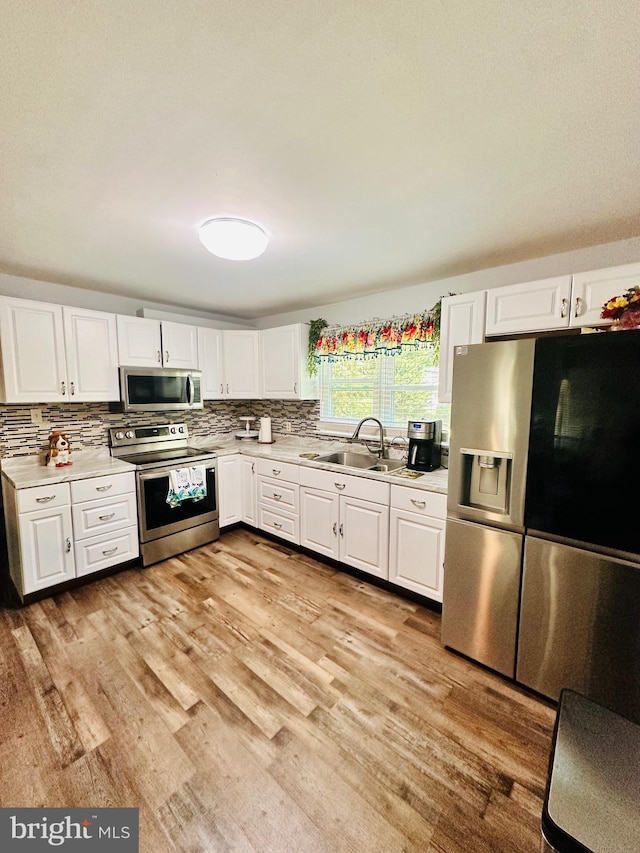 kitchen with white cabinetry, sink, stainless steel appliances, decorative backsplash, and light wood-type flooring