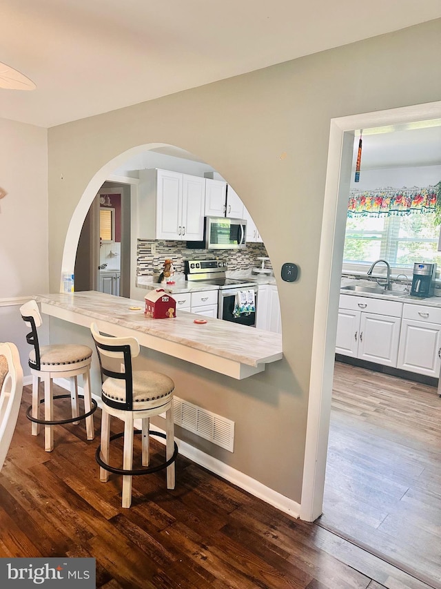 kitchen featuring appliances with stainless steel finishes, dark hardwood / wood-style floors, white cabinetry, and a breakfast bar area