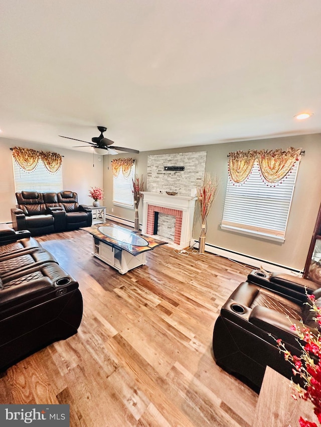 living room featuring ceiling fan, wood-type flooring, baseboard heating, and a brick fireplace