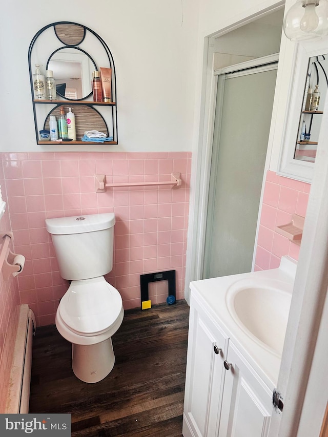 bathroom featuring vanity, a baseboard heating unit, hardwood / wood-style flooring, tile walls, and toilet