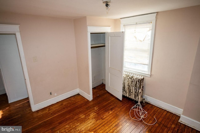 unfurnished bedroom with dark hardwood / wood-style floors, radiator heating unit, multiple windows, and a closet