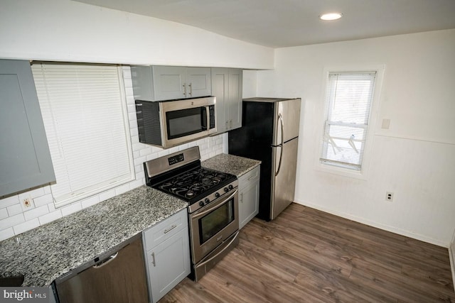 kitchen featuring light stone countertops, tasteful backsplash, dark hardwood / wood-style floors, gray cabinets, and appliances with stainless steel finishes