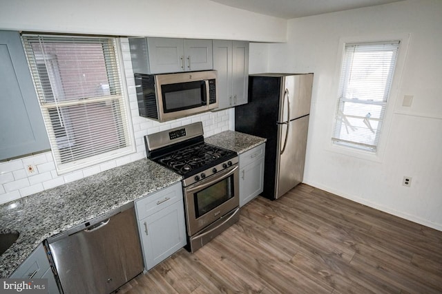 kitchen with dark wood-type flooring, backsplash, stone countertops, gray cabinets, and appliances with stainless steel finishes