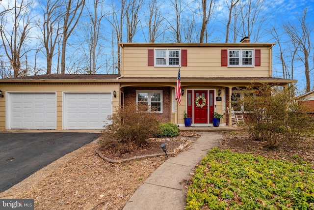 traditional-style house with a garage, a porch, brick siding, a chimney, and driveway