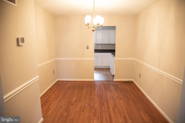 unfurnished dining area with dark wood-type flooring and an inviting chandelier