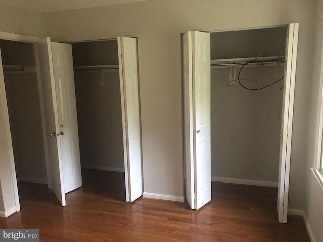 unfurnished bedroom with two closets and dark hardwood / wood-style floors