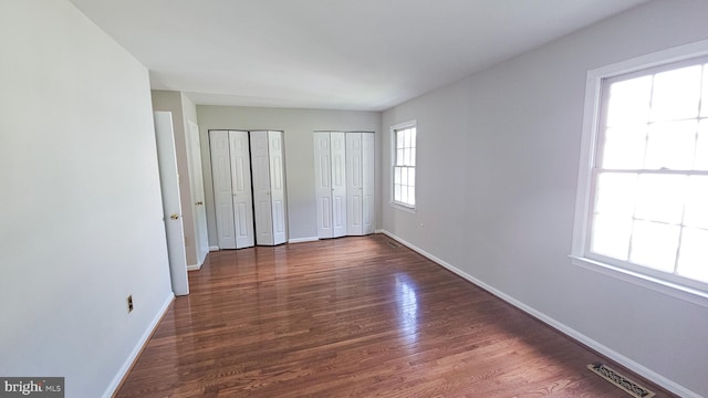 unfurnished bedroom with two closets and dark hardwood / wood-style floors