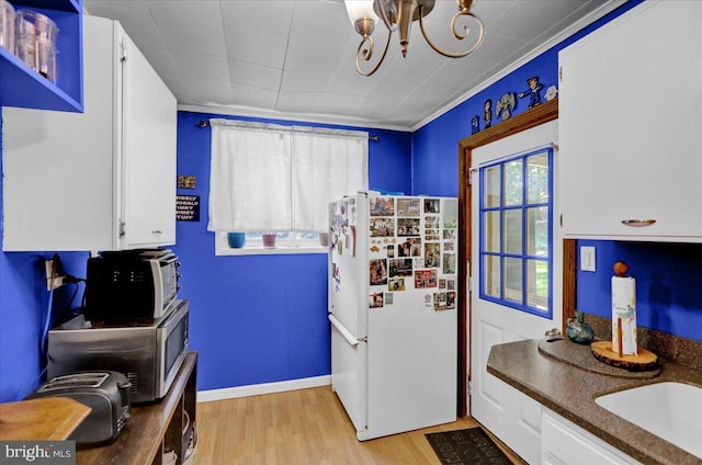 kitchen with light wood-type flooring, ornamental molding, white refrigerator, an inviting chandelier, and white cabinets