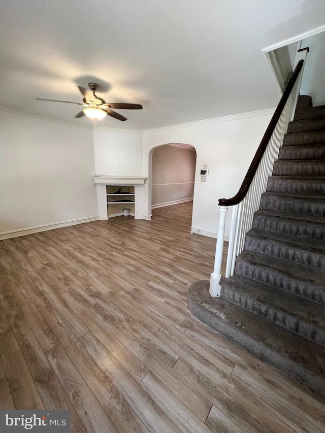 unfurnished living room featuring wood-type flooring, ornamental molding, and ceiling fan