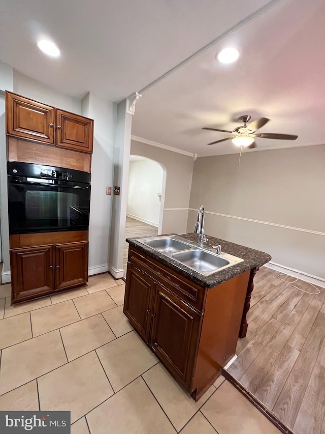 kitchen with light wood-type flooring, black oven, ceiling fan, sink, and ornamental molding