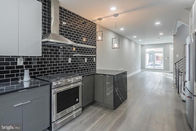 kitchen featuring stainless steel appliances, hanging light fixtures, light wood-type flooring, wall chimney exhaust hood, and backsplash