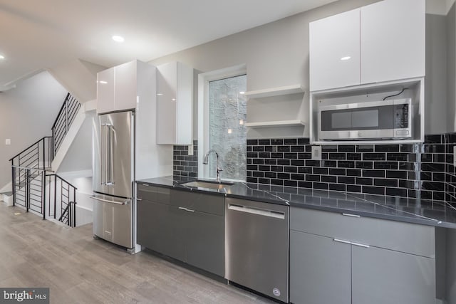 kitchen with tasteful backsplash, stainless steel appliances, white cabinets, sink, and light hardwood / wood-style floors