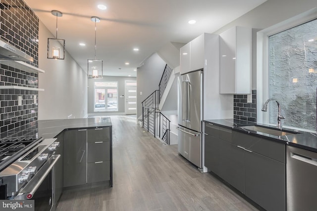 kitchen with premium appliances, white cabinetry, backsplash, light hardwood / wood-style floors, and pendant lighting