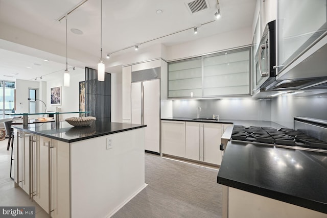 kitchen featuring sink, paneled built in fridge, white cabinetry, hanging light fixtures, and an island with sink