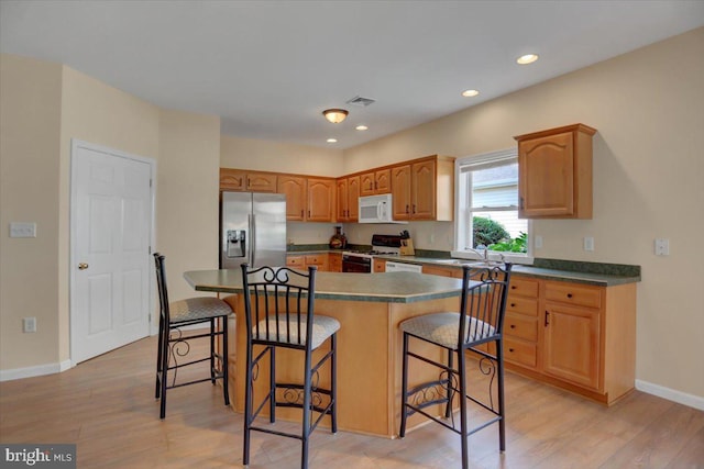 kitchen featuring sink, a breakfast bar area, a center island, light wood-type flooring, and white appliances