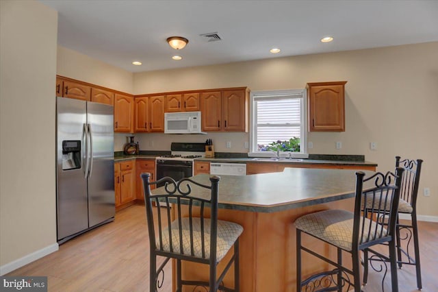 kitchen featuring sink, a breakfast bar area, a center island, white appliances, and light hardwood / wood-style flooring