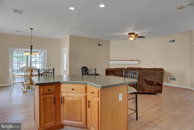 kitchen featuring a kitchen island, ceiling fan with notable chandelier, a breakfast bar area, hanging light fixtures, and light wood-type flooring