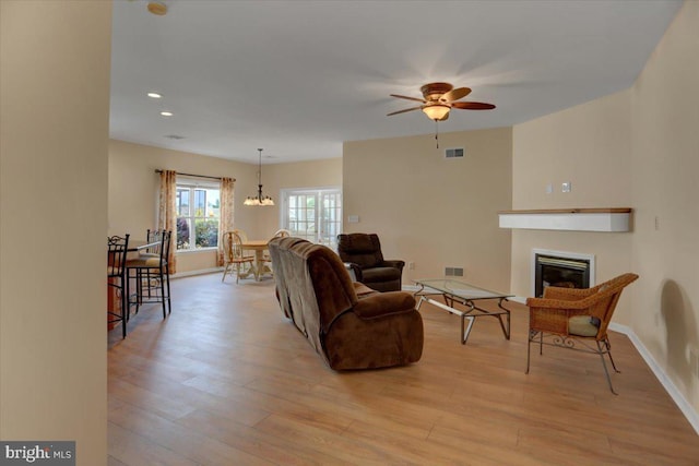 living room featuring ceiling fan with notable chandelier and light hardwood / wood-style floors