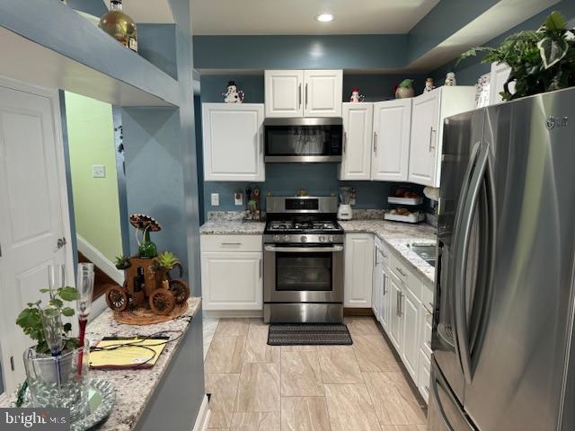 kitchen with white cabinets, light stone counters, and appliances with stainless steel finishes