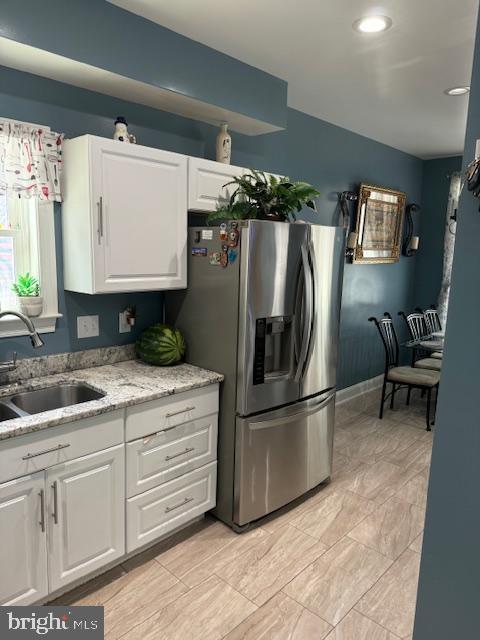 kitchen with white cabinets, sink, light stone countertops, and stainless steel refrigerator with ice dispenser