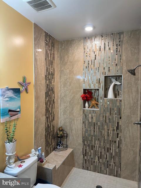 bathroom featuring tiled shower and toilet