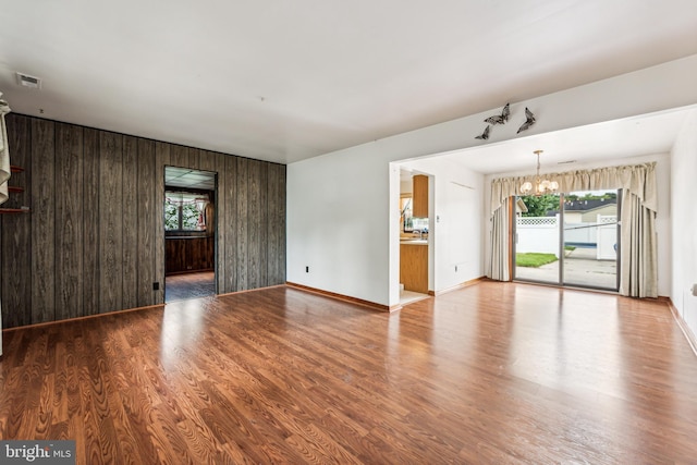 unfurnished living room featuring wood-type flooring, wooden walls, and a notable chandelier