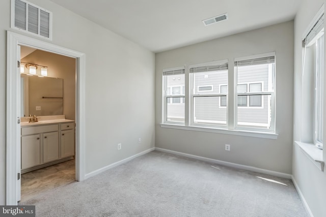 unfurnished bedroom featuring ensuite bath, sink, light colored carpet, and multiple windows