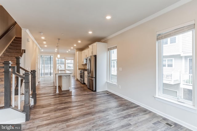 kitchen featuring white cabinetry, decorative light fixtures, a kitchen bar, a kitchen island with sink, and appliances with stainless steel finishes