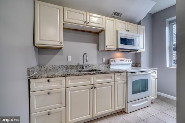 kitchen with sink, light stone counters, plenty of natural light, white appliances, and light tile patterned floors