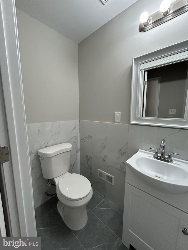 bathroom with vanity, toilet, and tile walls