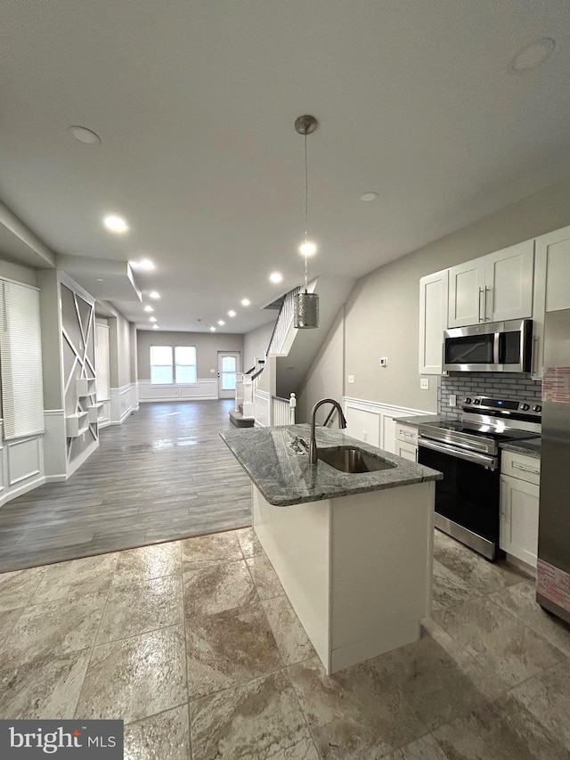 kitchen featuring white cabinetry, sink, an island with sink, dark stone counters, and appliances with stainless steel finishes