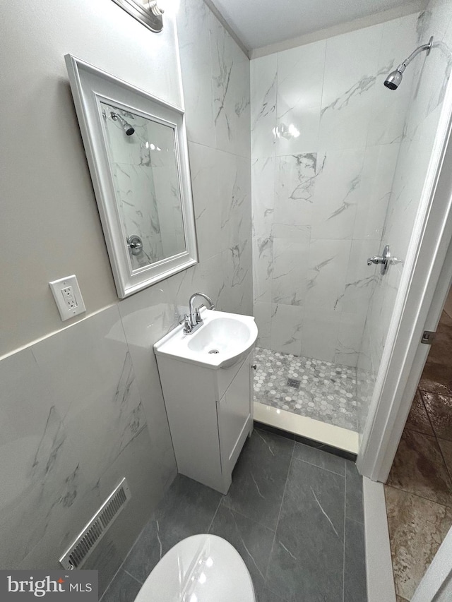 bathroom featuring a tile shower, vanity, toilet, and tile walls