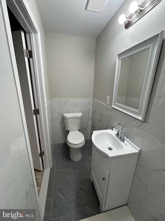 bathroom with vanity, toilet, and tile walls