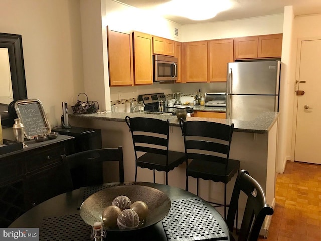 kitchen featuring a kitchen bar, kitchen peninsula, stone counters, and stainless steel appliances