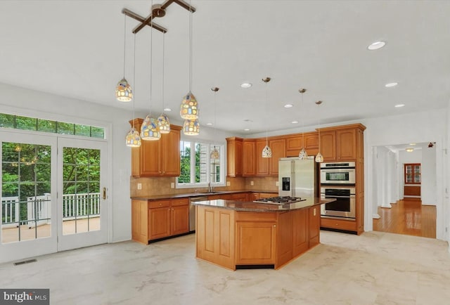 kitchen with hanging light fixtures, a center island, tasteful backsplash, dark stone counters, and appliances with stainless steel finishes