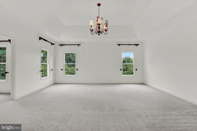 spare room with light colored carpet, a tray ceiling, and a chandelier