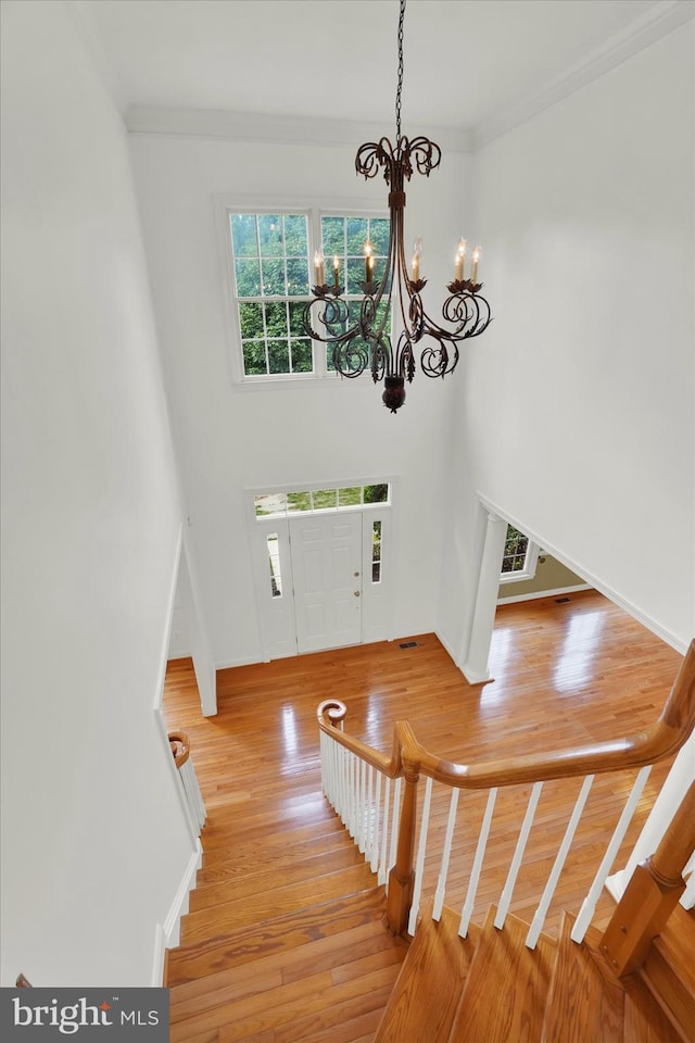 entryway with hardwood / wood-style floors, crown molding, and a notable chandelier