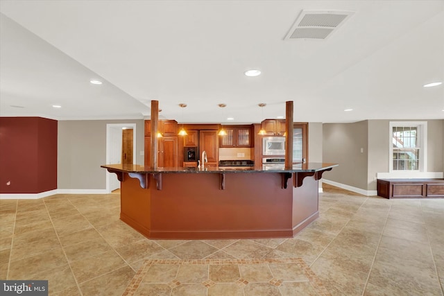 kitchen with pendant lighting, stainless steel appliances, a kitchen bar, dark stone counters, and sink