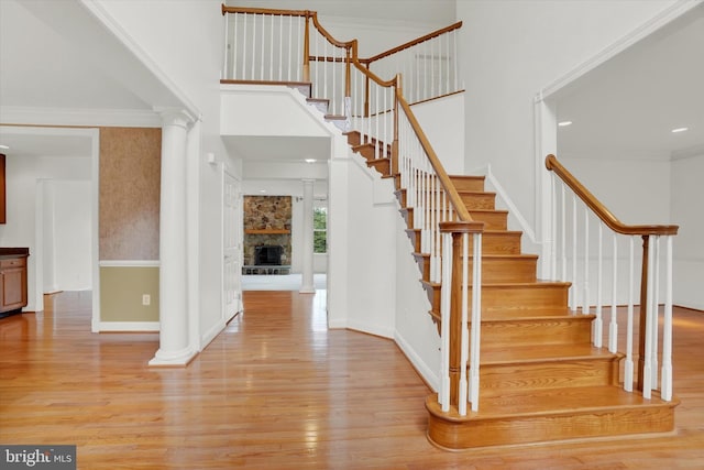 staircase featuring hardwood / wood-style floors, ornamental molding, and a stone fireplace