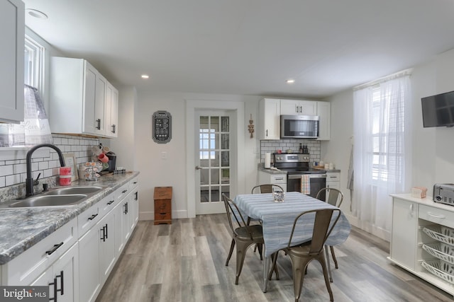 kitchen with backsplash, sink, light wood-type flooring, white cabinetry, and stainless steel appliances