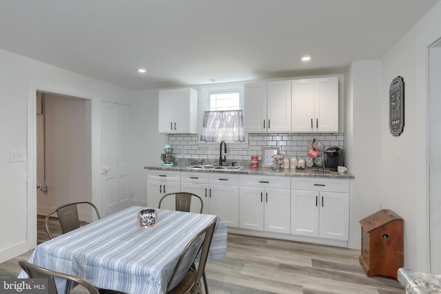 kitchen featuring light stone countertops, decorative backsplash, white cabinetry, and sink