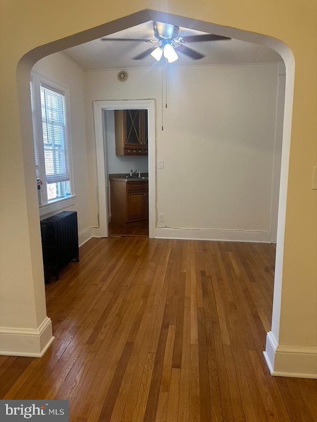 unfurnished living room featuring sink, radiator, wood-type flooring, and ceiling fan