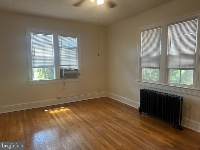 unfurnished room with radiator, a healthy amount of sunlight, and hardwood / wood-style floors