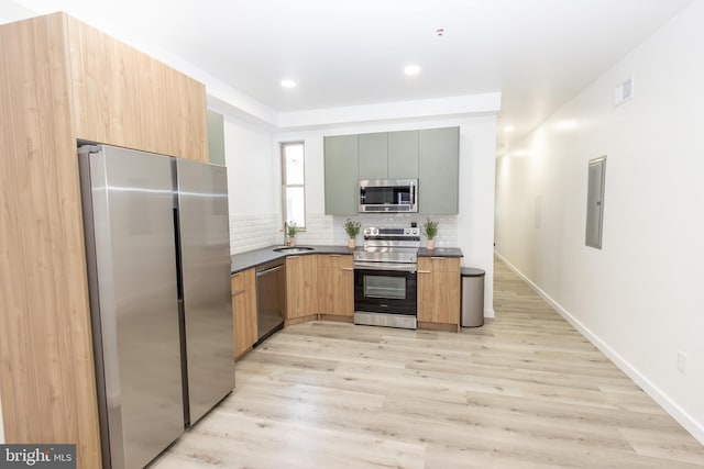 kitchen with sink, tasteful backsplash, electric panel, light hardwood / wood-style floors, and appliances with stainless steel finishes