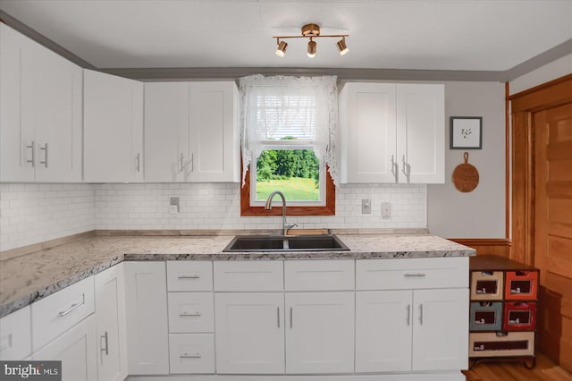 kitchen featuring tasteful backsplash, white cabinets, track lighting, hardwood / wood-style floors, and sink